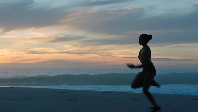 Active, sporty and fit woman running, sprinting or jogging on a beach during sunrise in summer. Dark silhouette of a fast, dedicated and energetic female athlete training, exercising and working out
