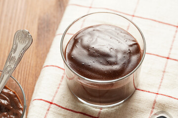Creamy french chocolate ganache or pudding in glass on linen napkin on wooden background