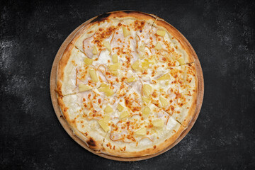 Pizza with meat, ham, pineapples, on a wooden round board on gray concrete. top view