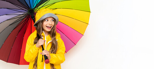 A little girl in a raincoat holds a multicolored umbrella on a white isolated background. Rainy...