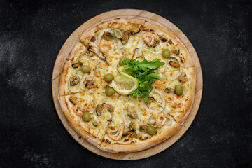 Marinara pizza with squid mussels shrimp olives and lemon, on a wooden round board on gray concrete. top view