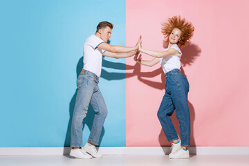 Fototapeta premium Portrait of young, emotive couple, man and woman, dancing, posing isolated over pink blue studio background