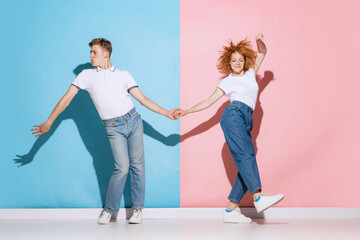 Portrait of young couple holding hands, dancing boogie woogie isolated over pink blue studio...