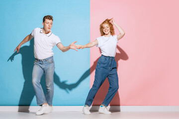 Naklejka premium Portrait of young beautiful couple, cheerfully dancing isolated over pink blue studio background. Happy celebration