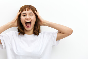 funny, very emotional woman screams loudly clutching her head while standing in a white T-shirt on a light background