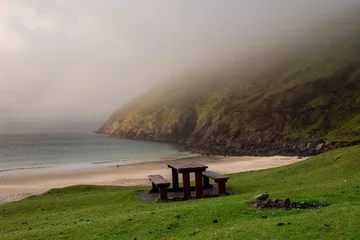 Wall murals Camps Bay Beach, Cape Town, South Africa Table and benches for tourist on a grass with stunning view on Keem bay and beach early in the morning. Low clouds and fog over ocean and mountain. Ireland. Famous travel area. Irish landscape.