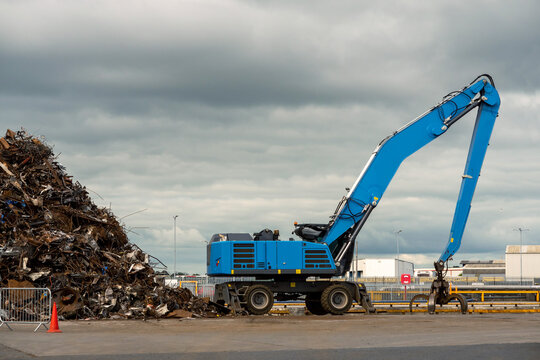 Blue excavator with claw arm in a scrap metal yard. Metal recycling industry. Export of junk for profit and ecology. Port area.