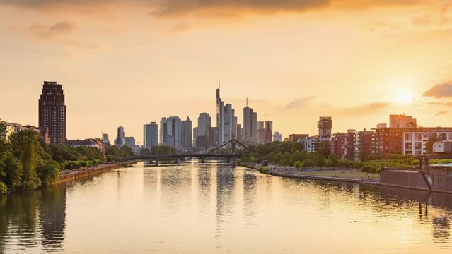 Sunset Frankfurt skyline time lapse, blue sky with clouds, office buildings and skyscraper in center with river and bridges in the foreground, Frankfurt am Main, Hessen, Germany