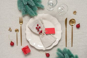 Christmas table setting with golden cutlery on a beige textile background. Linen beige napkin with...