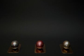 Photography of three festive Easter chicken eggs painted with golden black and red colour lie on a small golden stand on a black background. Ready for the happy holidays. No people photography