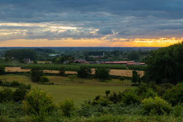 Fototapeta premium Colourful sunrise in the only Dutch mountain village located in the south of Limburg, with a view on a spectacular sky, the tower of the catholic church , the vineyards and agricultural grain fields 