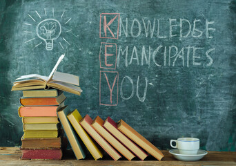 books and blackboard with drawing of a lightbulb and slogan knowledge emancipates...