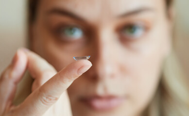 Focus on finger, young woman holding a contact lens in front of her face