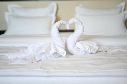 Swans made of white bath towel in hotel room. Decoration on bed in motel. Towel folded in swan shape. 