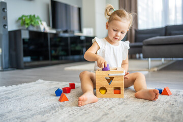 Cute caucasian little girl playing on the floor at home with eco wooden toys. The child playing educational games.