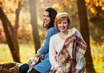 Fototapeta premium Portrait of two beautiful smiling women wrapped in blanket in autumn forest