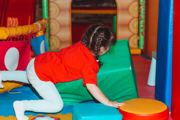 A happy little girl is having fun in an indoor play center. A child plays with colored balls in a...
