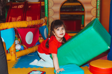 A happy little girl is having fun in an indoor play center. A child plays with colored balls in a pool with a ball on the playground.