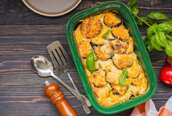 Moussaka, a layered casserole of eggplant, potatoes, tomatoes and minced meat in a green ceramic form on a brown wooden background. Rustic style.