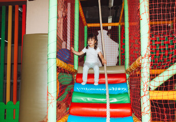 A happy little girl is having fun in an indoor play center. A child plays with colored balls in a pool with a ball on the playground.