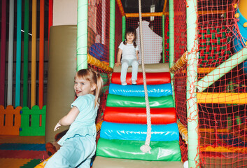 A happy little girl is having fun in an indoor play center. A child plays with colored balls in a...