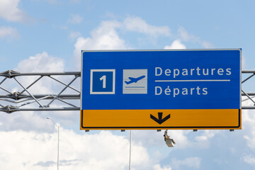 Airport Departures (English/French) sign above roadway on partly cloudy day. 