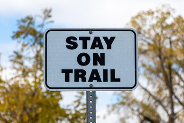 "Stay On Trail" metal black and white sign on a sunny fall day. 