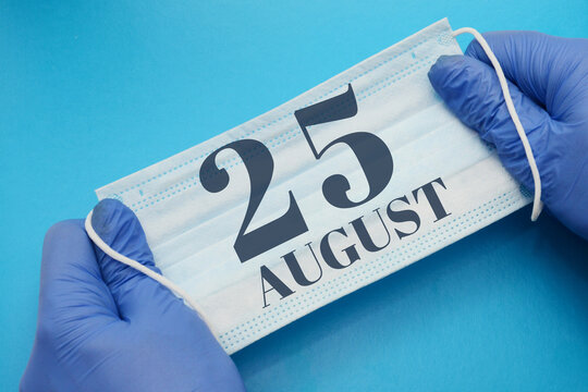 25 august day of month. Doctor holding an antivirus mask in blue medical gloves on blue background. Protection from disease