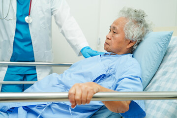 Asian elder senior woman patient holding bed rail while lie down with hope waiting her family in...