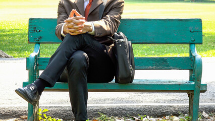 Asian young business man sitting on a wooden bench and relaxing in the park