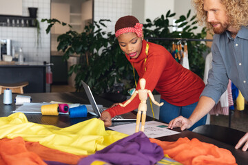 Multiracial male and female fashion designers discussing over sketch at desk in studio office