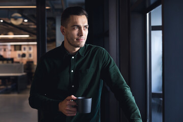 Thoughtful caucasian young businessman with coffee cup at creative office