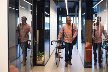 Caucasian mature businessman walking with bicycle in corridor of creative office - Powered by Adobe