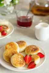 Close-up of cheesecakes with strawberries on a white plate on the table. Breakfast on a sunny day.