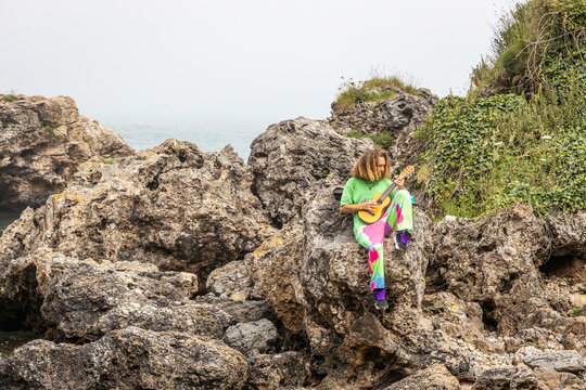 Talented male guitarist playing ukulele on rocky cliff