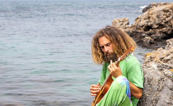 Talented male guitarist playing ukulele on rocky cliff