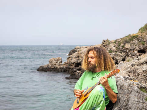 Talented male guitarist playing ukulele on rocky cliff