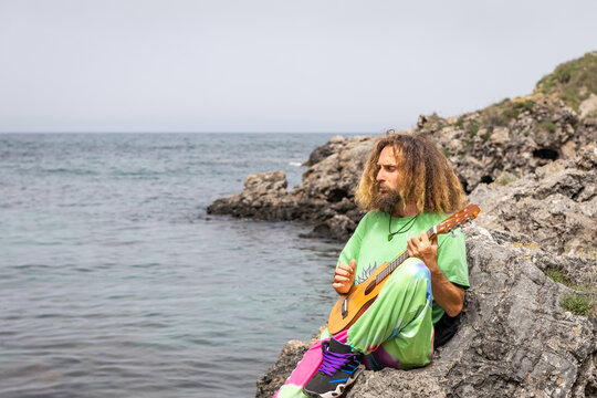 Talented male guitarist playing ukulele on rocky cliff