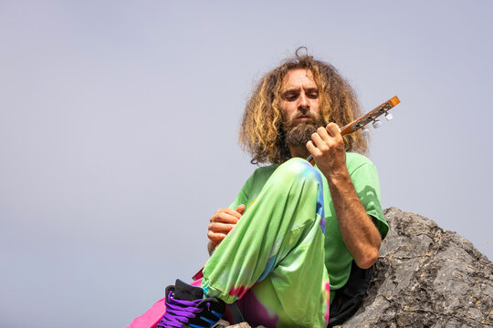 Talented male guitarist playing ukulele on rocky cliff