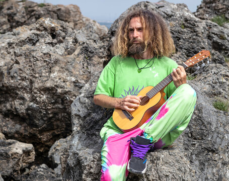 Talented male guitarist playing ukulele on rocky cliff
