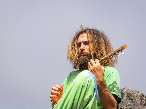 Talented male guitarist playing ukulele on rocky cliff