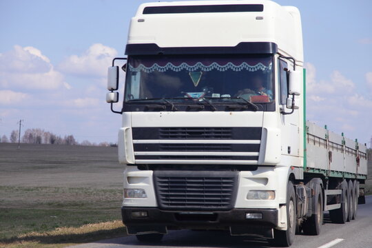 White Euro semi truck with empty lowbed trailer on country road front view