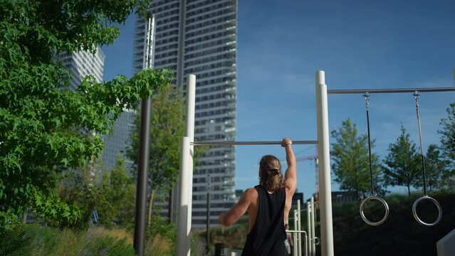 Back view of male sportsman doing pull ups on the horizontal bar while training outdoors