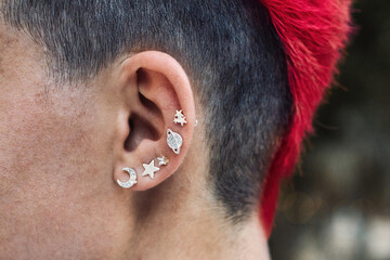 Closeup of a female punk's ear with silver piercings and a bright red dyed mohawk personal hair style - obrazy, fototapety, plakaty