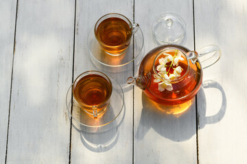 Flowers Jasmine in glass teapot and tea in cups on a wooden white background, natural light photo with hard shadows. Cup with green jasmin tea