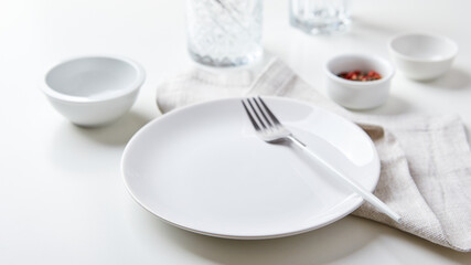 Empty white plate with a fork and small bowls on a light background