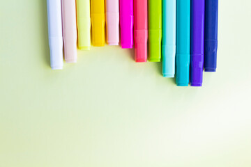 Multi-colored markers for sketching, for drawing drawings and objects, for working in the office and studying at school, are folded in waves with closed caps on a light yellow background.