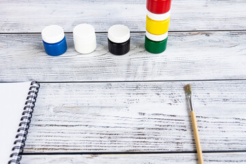 A sketchbook with white sheets, paint brushes and colorful, bright gouache paints on a light, gray...