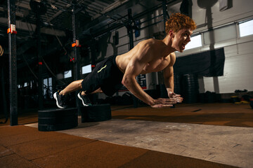 Portrait of young sportive man with muscular body training, doing push-ups exercises isolated over...