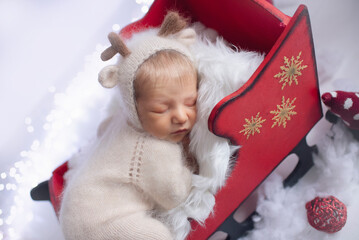 Beautiful newborn baby sleeps in santa claus sleigh dressed as deer